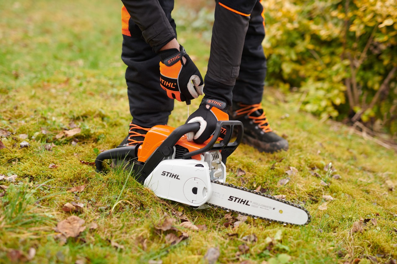 Una motosierra STIHL arranque fácil MS 180 C-BE en el suelo, sujetada por el asa por una persona con guantes protectores