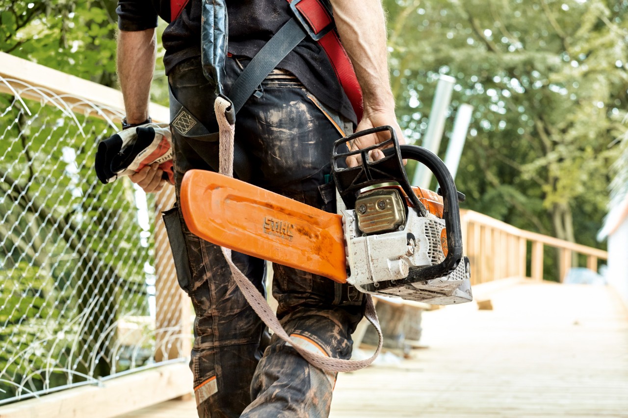 Una motosierra de gasolina STIHL MS 261 con protector de cadena que transporta un hombre mientras camina por un puente
