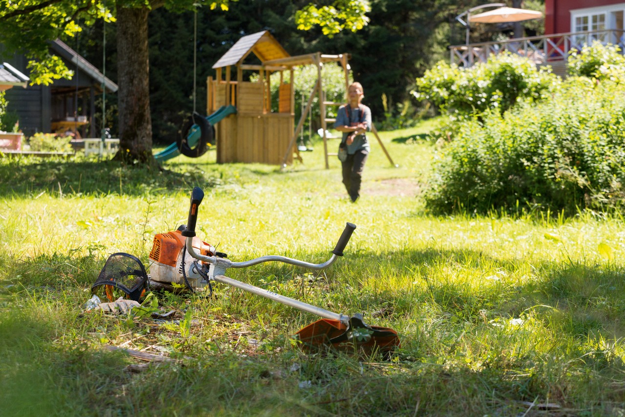 Una motoguadaña STIHL FS 240 está sobre la hierba; en segundo plano un hombre se prepara para realizar el mantenimiento