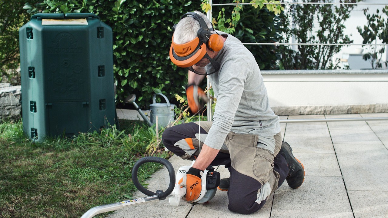 Una persona con ropa de protección tira de la cuerda de arranque de la desbrozadora de gasolina STIHL FS 38