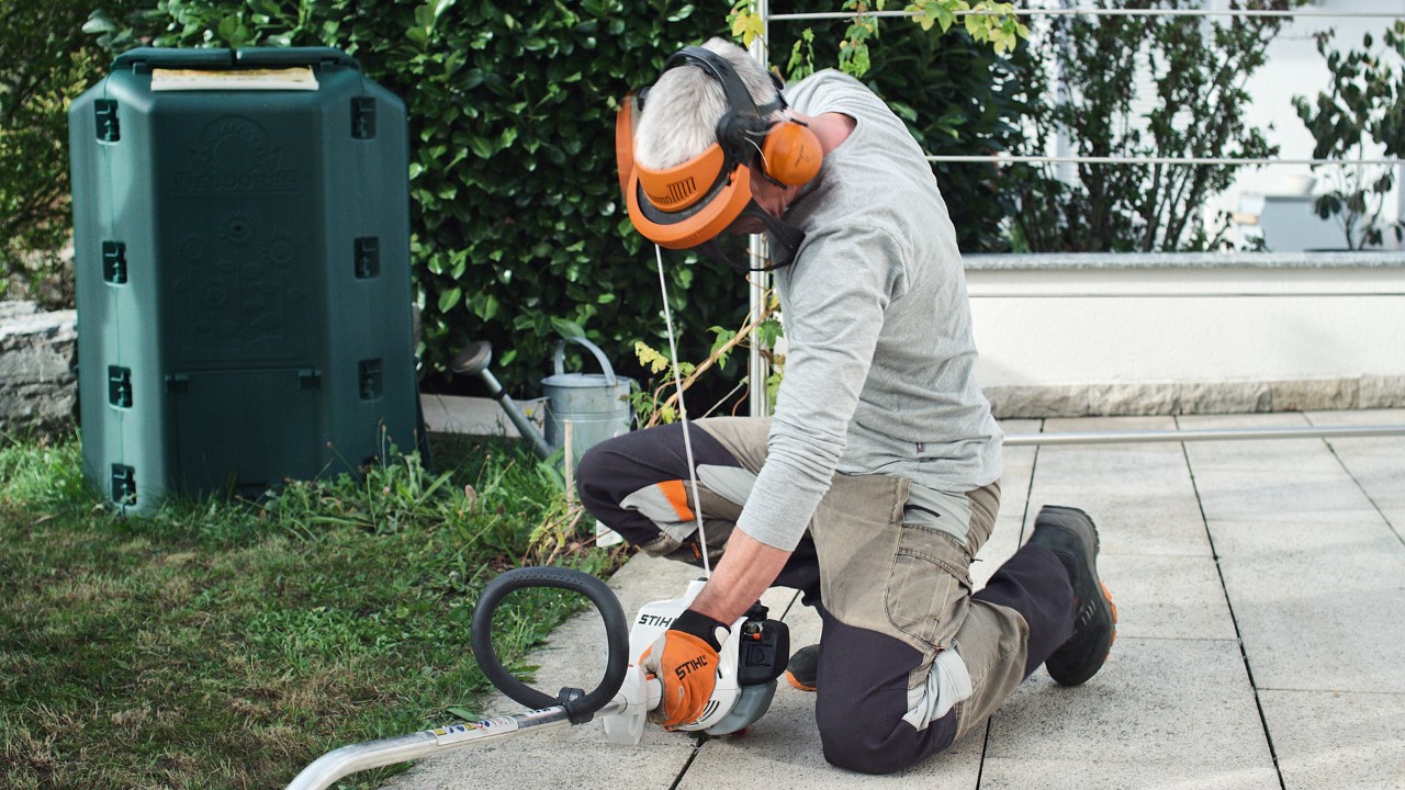 Una persona con ropa de protección vuelve a tirar de la cuerda de arranque de la desbrozadora de gasolina STIHL FS 38