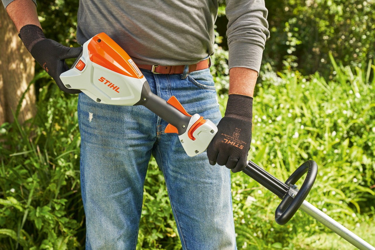 Un hombre con guantes de protección comprueba la batería de la desbrozadora STIHL FSA 60 para arrancarla