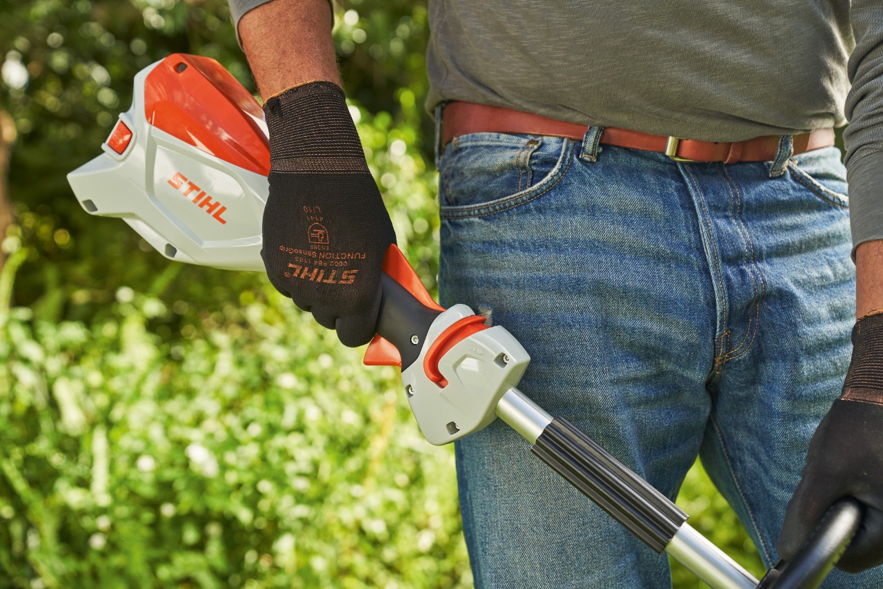 Un hombre con guantes de protección suelta la palanca de cambio de la desbrozadora de batería STIHL FSA 60 para pararla
