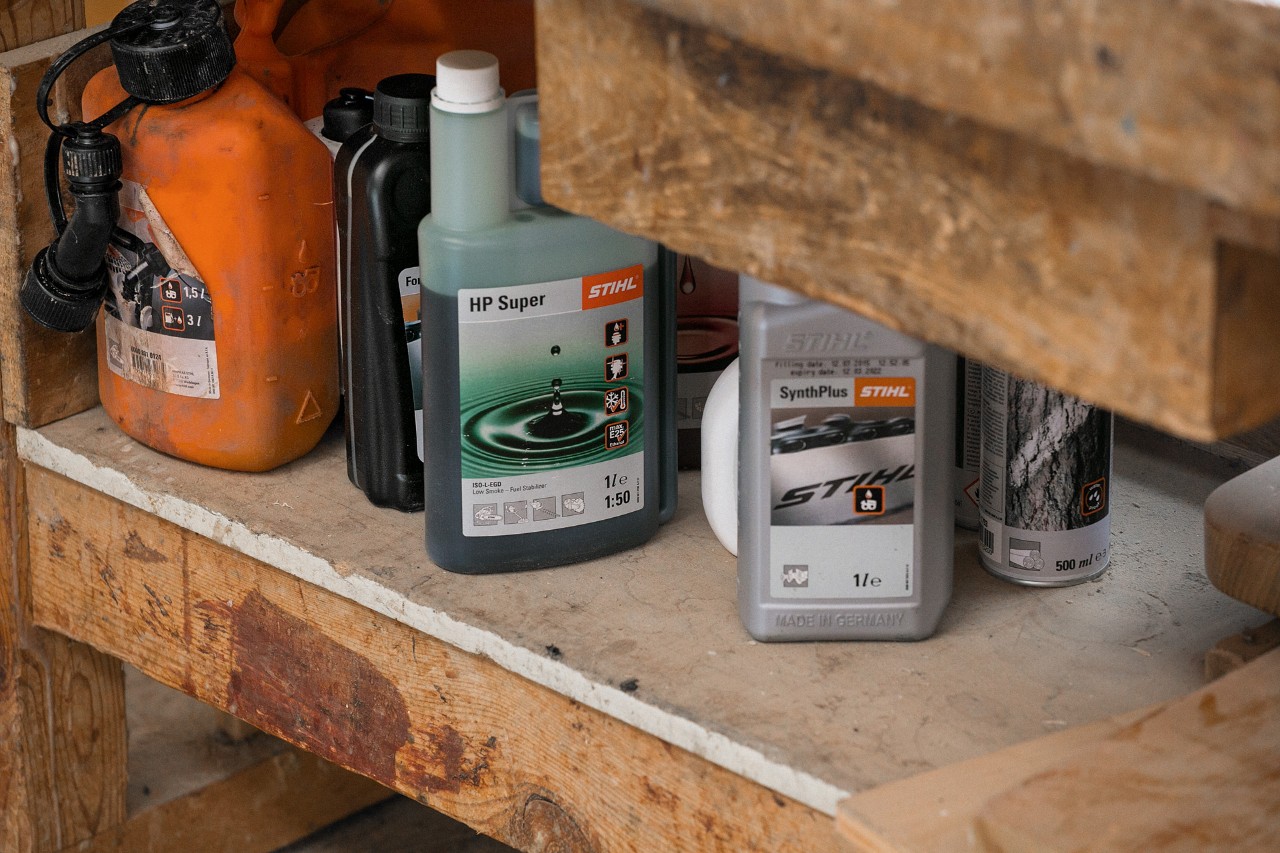 Aceite adhesivo de cadena STIHL SynthPlus y aceite de motor STIHL HP Super junto a otros materiales consumibles en una estantería