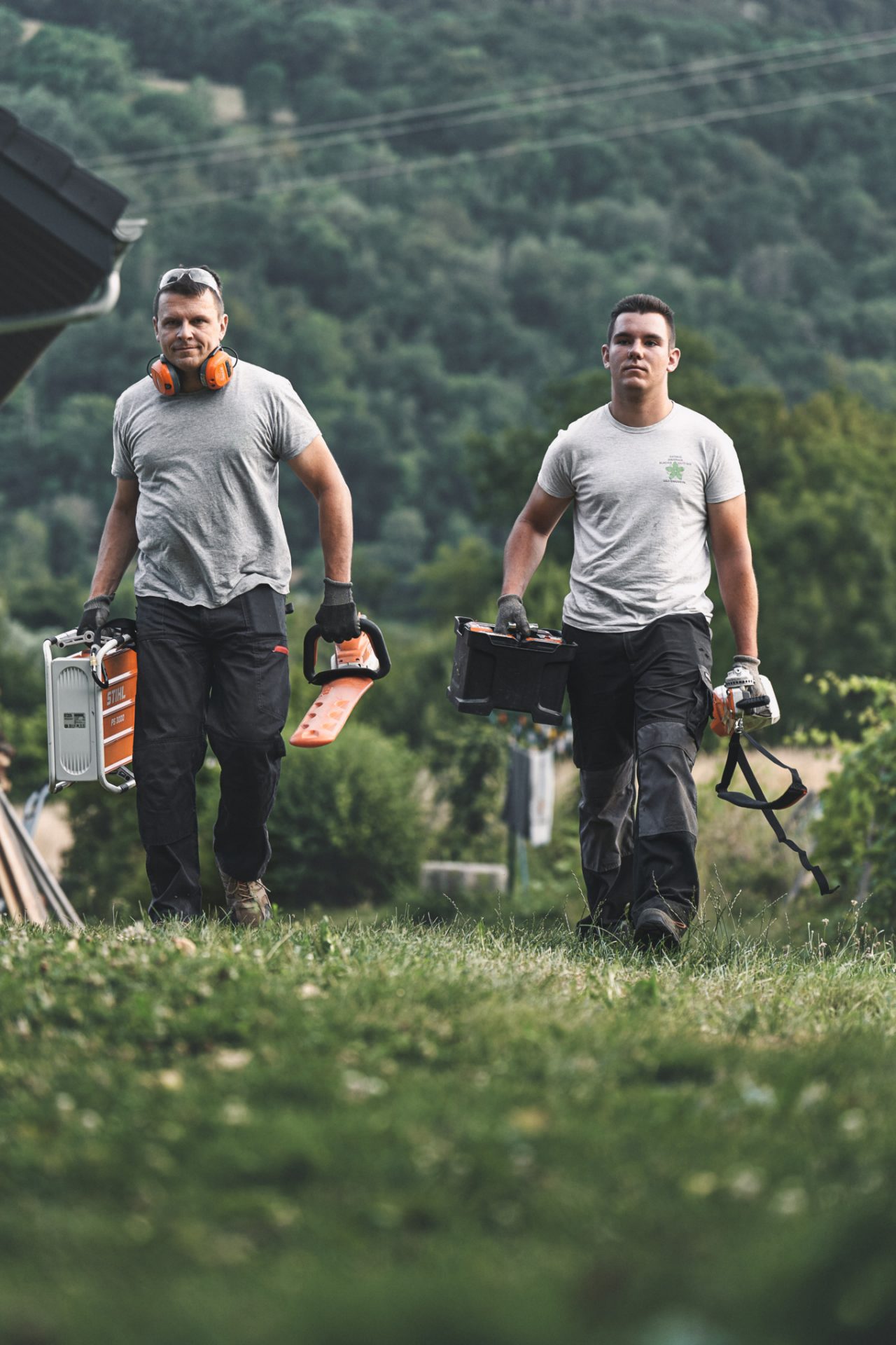 Dos profesionales caminan por un prado con máquinas de batería STIHL