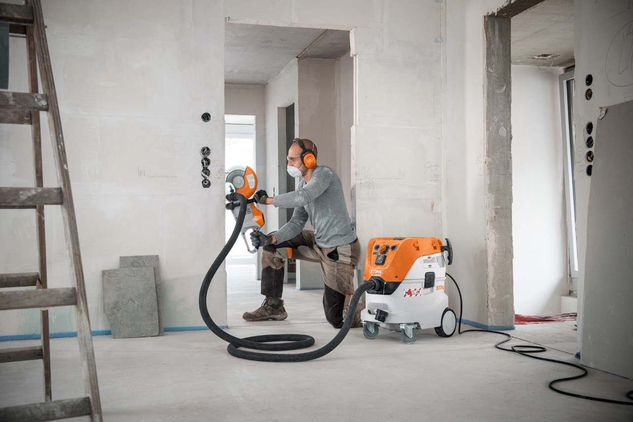 Un hombre utiliza un aspirador de sólidos y líquidos STIHL SE 133 ME mientras trabaja con una máquina de corte STIHL TSA 230