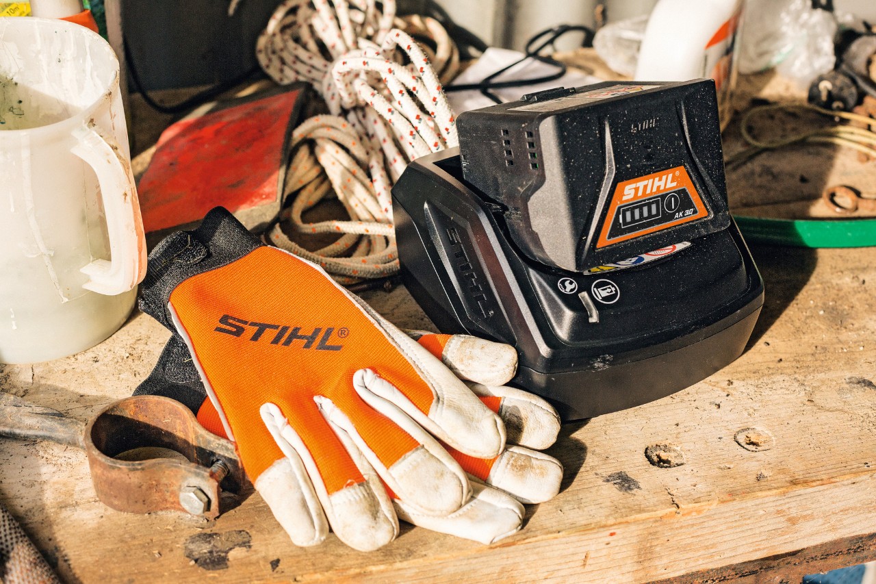 Sobre una superficie de trabajo reposan una batería y unos guantes