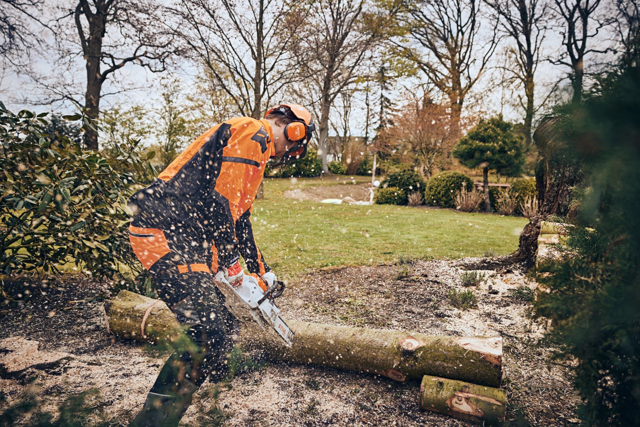 Un hombre con equipamiento de protección corta un tronco en una zona verde con una motosierra a batería STIHL